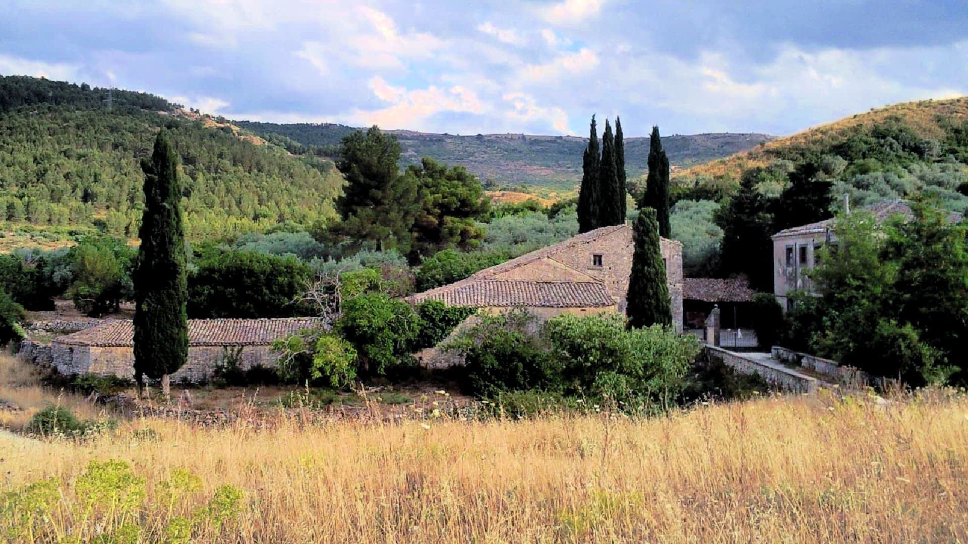 A stone building with a tiled roof, surrounded by trees and tall grass in a rural landscape. - Olive Oil Times