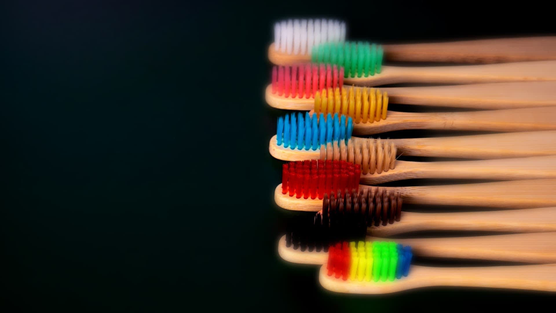 A row of bamboo toothbrushes with various colored bristles arranged in a line. - Olive Oil Times