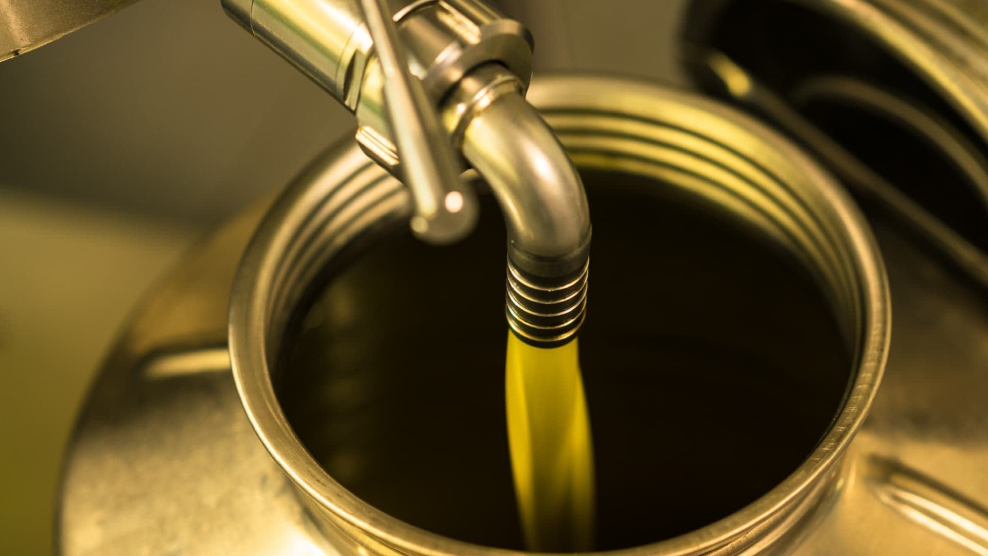 Olive oil being poured from a metal canister into a container. - Olive Oil Times