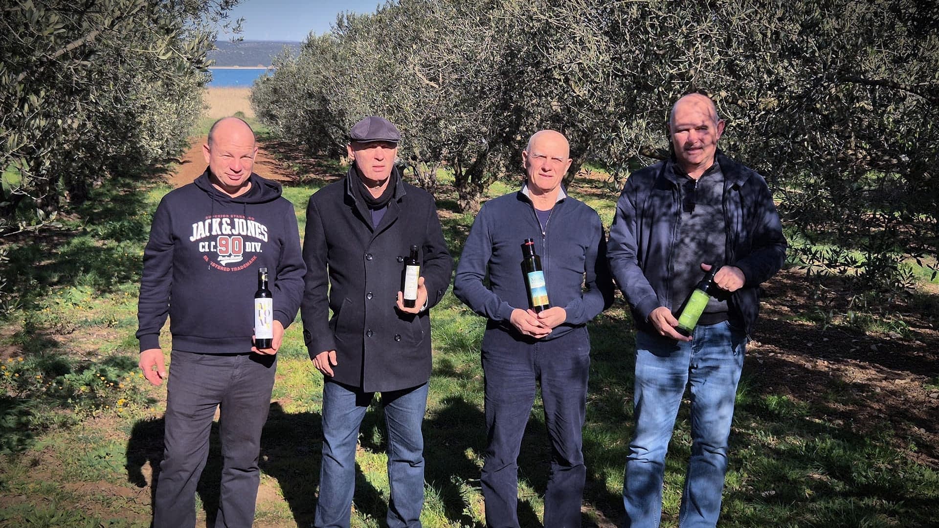 Four men standing in an olive grove, each holding a bottle of olive oil. - Olive Oil Times