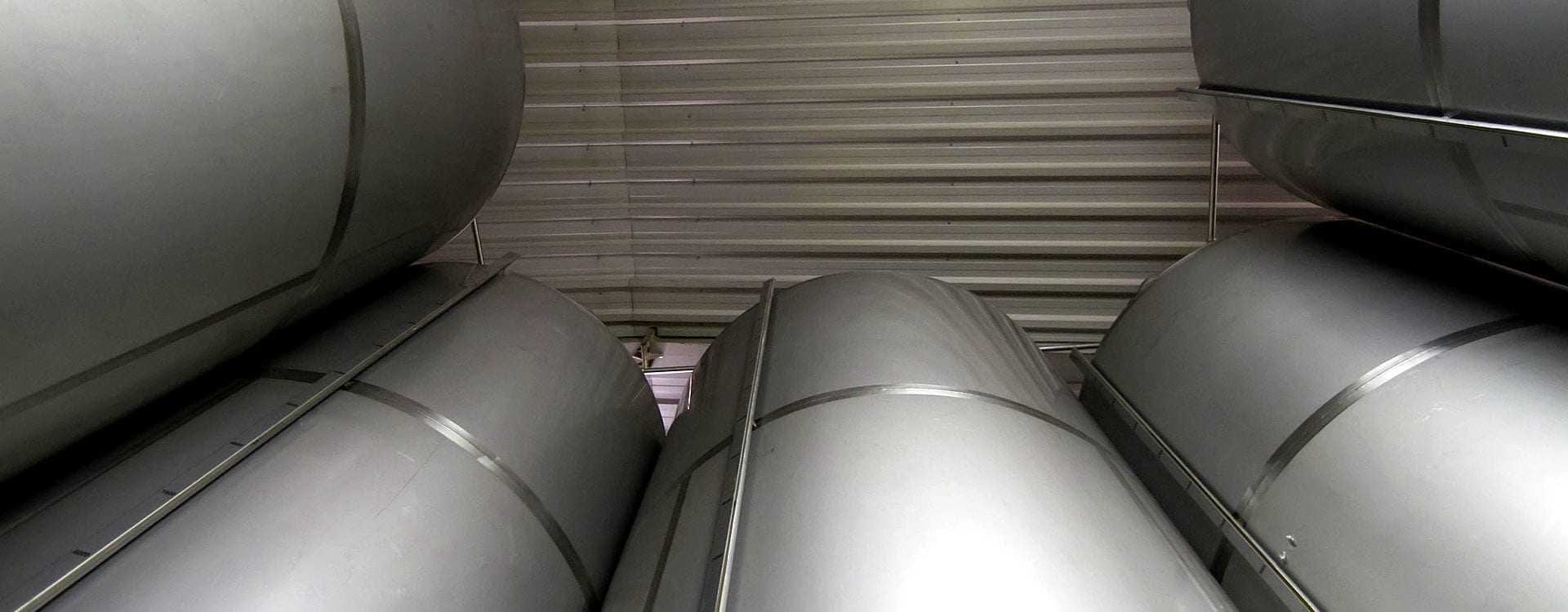 Stacked metal storage tanks in a warehouse with a metallic finish and cylindrical shape. - Olive Oil Times