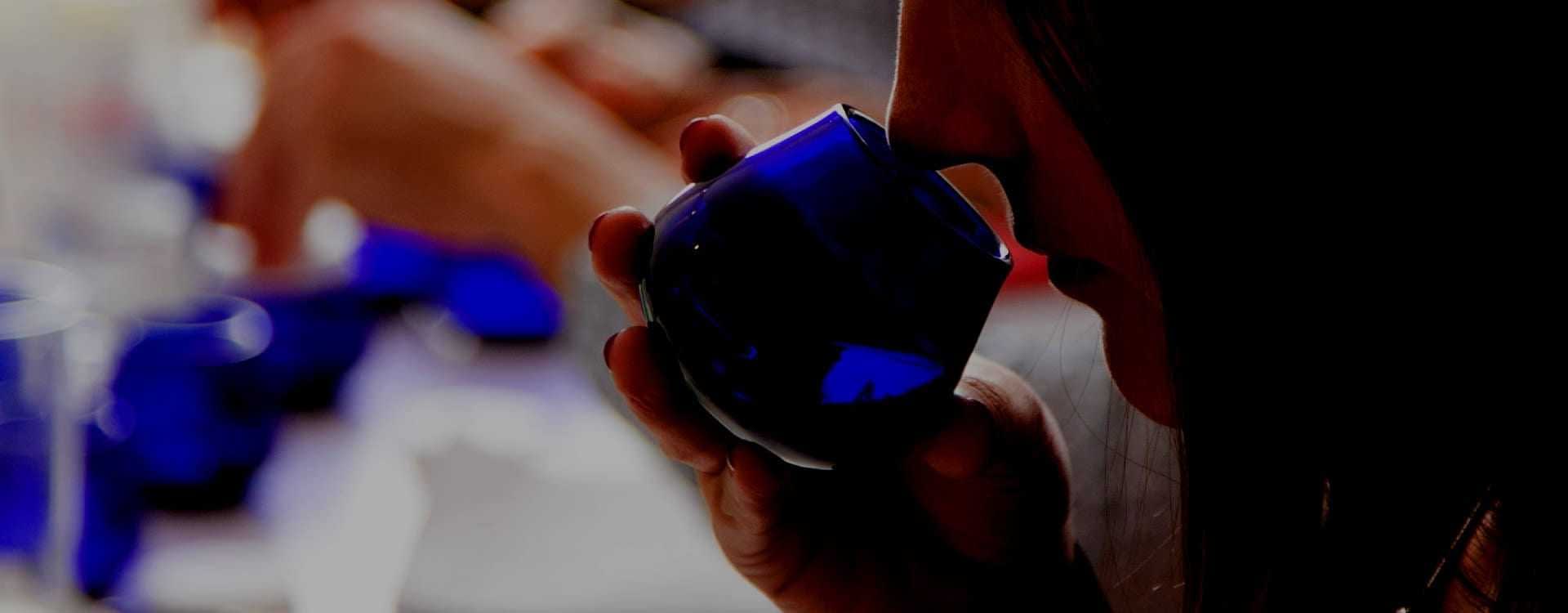 Individual holding a blue glass container while smelling olive oil during a tasting session. - Olive Oil Times