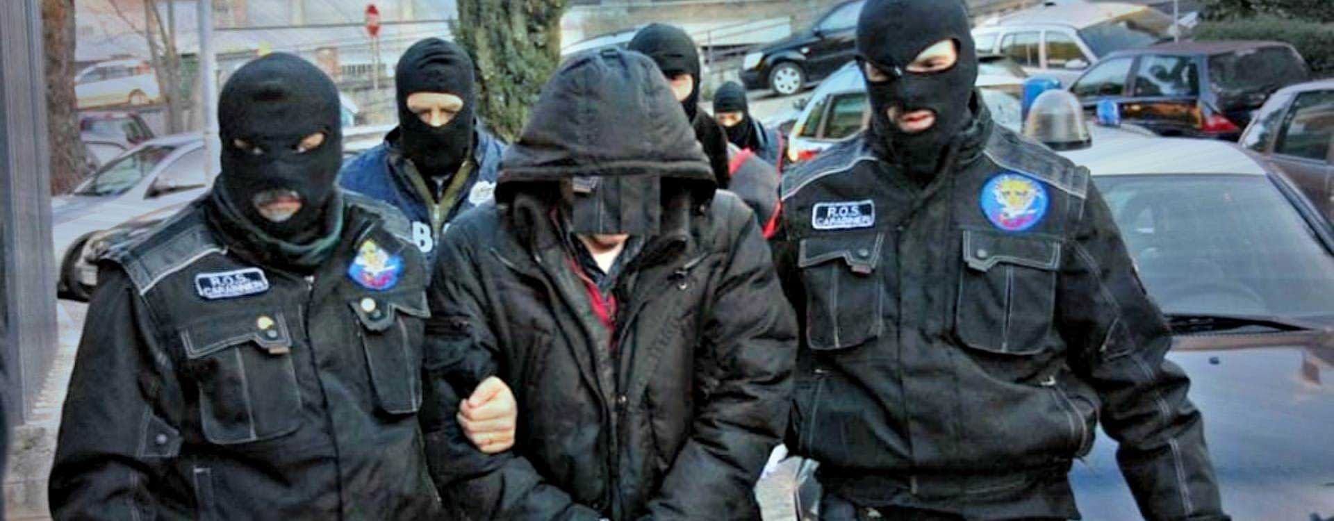 Police officers in tactical gear escorting an individual wearing a hooded jacket. - Olive Oil Times