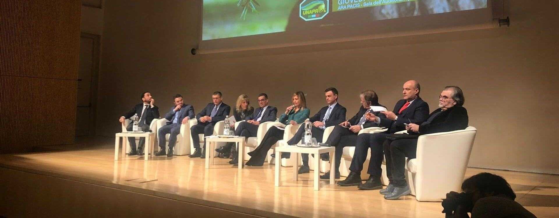 A panel of speakers seated on stage during a conference event, discussing various topics. - Olive Oil Times