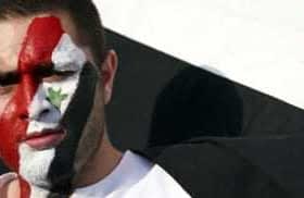 Man with Syrian flag face paint and holding a Syrian flag during a demonstration. - Olive Oil Times