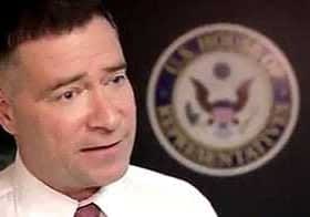 Man in a white shirt and tie speaking in front of a U.S. government seal. - Olive Oil Times