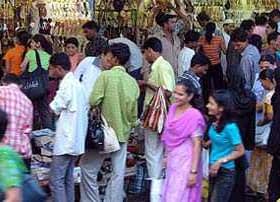 A busy market scene with a diverse group of people shopping and browsing various items. - Olive Oil Times