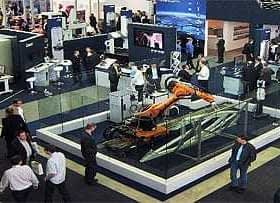 An exhibition booth featuring a robotic arm and various displays with attendees interacting. - Olive Oil Times
