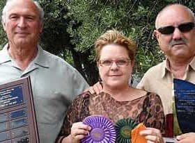 Three individuals posing together, holding various awards and ribbons in their hands. - Olive Oil Times