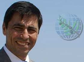 Man wearing a suit and smiling against a clear sky background with a globe graphic. - Olive Oil Times