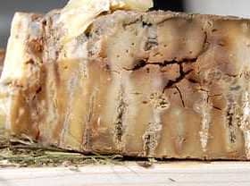 A block of aged cheese with a textured surface placed on a wooden board. - Olive Oil Times