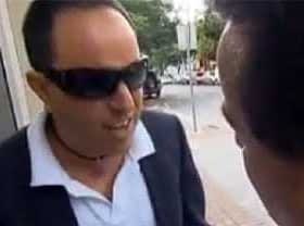 Man wearing sunglasses and a blazer engaged in conversation with another individual. - Olive Oil Times