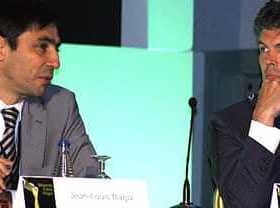 Dva moška med razpravo sedita za konferenčno mizo, eden v obleki, drugi v blazerju. - Olive Oil Times