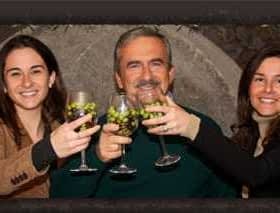 Three individuals, two women and one man, raising glasses filled with grapes in a celebratory manner. - Olive Oil Times