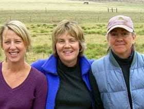 Three women standing together outdoors, smiling at the camera with a grassy background. - Olive Oil Times