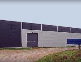Large industrial warehouse building with a gray and black exterior and a loading dock area. - Olive Oil Times