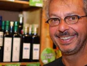 Man with glasses smiling in front of shelves displaying olive oil bottles. - Olive Oil Times