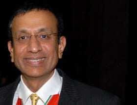 A man wearing a black suit and a tie, smiling at the camera in a formal setting. - Olive Oil Times