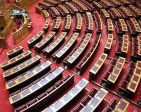 Interior view of the Greek Parliament chamber featuring rows of wooden seating and a red carpet. - Olive Oil Times