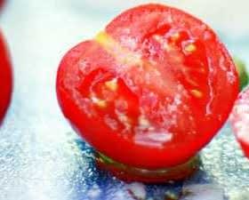 A halved tomato showing its interior with seeds and flesh visible on a reflective surface. - Olive Oil Times