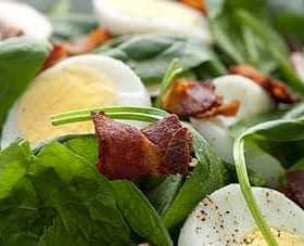 A bowl of salad containing spinach, sliced hard-boiled eggs, and pieces of bacon. - Olive Oil Times