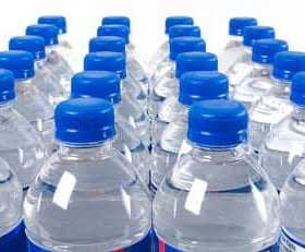 Multiple plastic bottles of water with blue caps arranged in rows. - Olive Oil Times