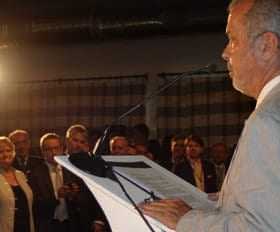 A man in a light-colored suit speaking at a podium while an audience listens attentively. - Olive Oil Times