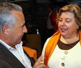 Two individuals, one wearing an orange scarf, engaged in a conversation at an indoor event. - Olive Oil Times