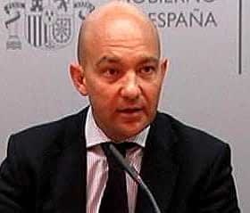 A man in a suit speaking at a press conference with a microphone in front of him. - Olive Oil Times