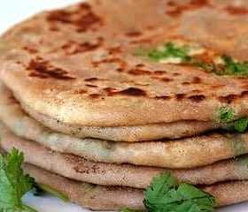 A stack of paratha bread garnished with fresh cilantro leaves on a white plate. - Olive Oil Times
