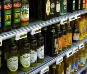 Multiple bottles of olive oil displayed on shelves in a grocery store. - Olive Oil Times