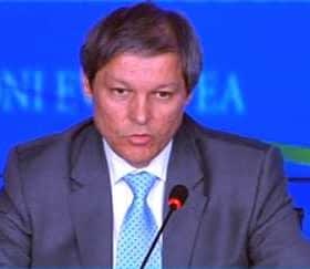 A man in a suit speaking at a podium during a conference with a blue backdrop. - Olive Oil Times