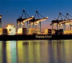 Un grand porte-conteneurs nommé Hapag-Lloyd a accosté dans un port avec des grues illuminées au crépuscule. - Olive Oil Times