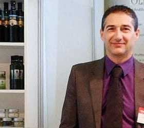 Ein Mann im Anzug steht vor einer Auslage mit Olivenölprodukten in Regalen. - Olive Oil Times