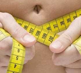 Person holding a yellow tape measure around their waist, showing measurement of body size. - Olive Oil Times