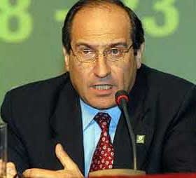 A man in a suit speaking at a podium with a microphone during a conference. - Olive Oil Times