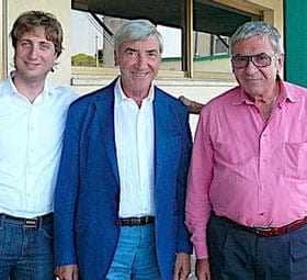 Three men standing together, one in a blue blazer, one in a white shirt, and one in a pink shirt. - Olive Oil Times
