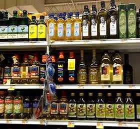 Multiple bottles of olive oil displayed on a grocery store shelf in various sizes and brands. - Olive Oil Times