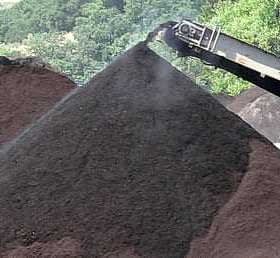 Conveyor belt transferring black soil to a pile in an outdoor setting. - Olive Oil Times