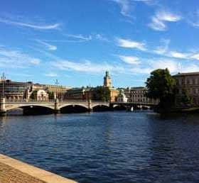 Vue d'un pont sur l'eau à Stockholm avec des bâtiments et des arbres en arrière-plan. - Olive Oil Times