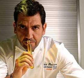 Chef holding a culinary tool while looking directly at the camera in a professional kitchen setting. - Olive Oil Times