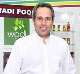 Man in a white shirt standing in front of Wadi Food branding and product display. - Olive Oil Times