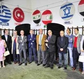 A group of individuals standing in a meeting room with flags displayed on the wall behind them. - Olive Oil Times