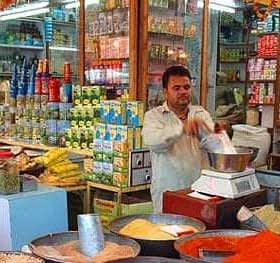 A shop displaying a variety of spices and packaged goods with a man measuring ingredients. - Olive Oil Times