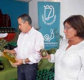 Two individuals examining bottles of olive oil at a display with branding in the background. - Olive Oil Times