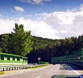 A highway with a green sound barrier on one side and trees in the background under a partly cloudy sky. - Olive Oil Times