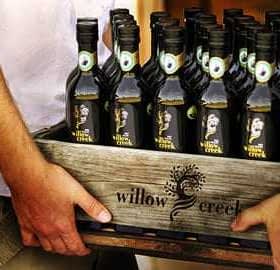 Una cassa di legno piena di bottiglie di olio d'oliva Willow Creek tenuta da due persone. - Olive Oil Times