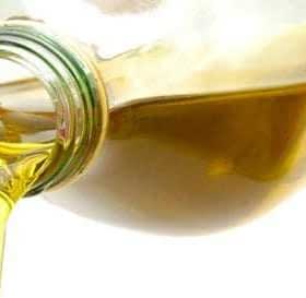 A glass bottle pouring olive oil with a clear stream of liquid flowing from the spout. - Olive Oil Times