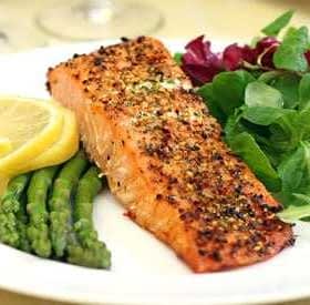 Grilled salmon fillet served with asparagus, lemon slices, and mixed salad greens on a white plate. - Olive Oil Times