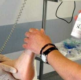 Medical professional applying a spray treatment to a patient's leg in a clinical setting. - Olive Oil Times